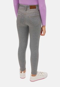 Leggings grises con una textura suave, diseño ajustado y bolsillos traseros. Presenta una etiqueta de marca de cuero marrón en la cinturilla.