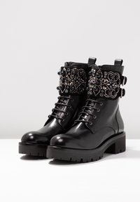 Stivali neri in pelle con cavigliera e suola spessa, caratterizzati da intricate decorazioni in perline e strass sulla fascia superiore e sulle fibbie laterali.