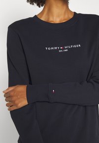 Felpa navy in misto cotone, con polsini e scollatura a costine. Include il logo ricamato "TOMMY HILFIGER EST. 1985" sul davanti.