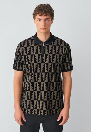 Kortærmet polo-shirt i sort og tan med geometrisk lynmønster. Har en lynlåskrave og kontrasterende sorte manchetter.