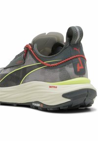 Chaussure de course PUMA avec une tige en mesh grise, des accents rouges, un contour jaune, une épaisse semelle intermédiaire blanche et une semelle extérieure en caoutchouc noire avec des détails de marque.