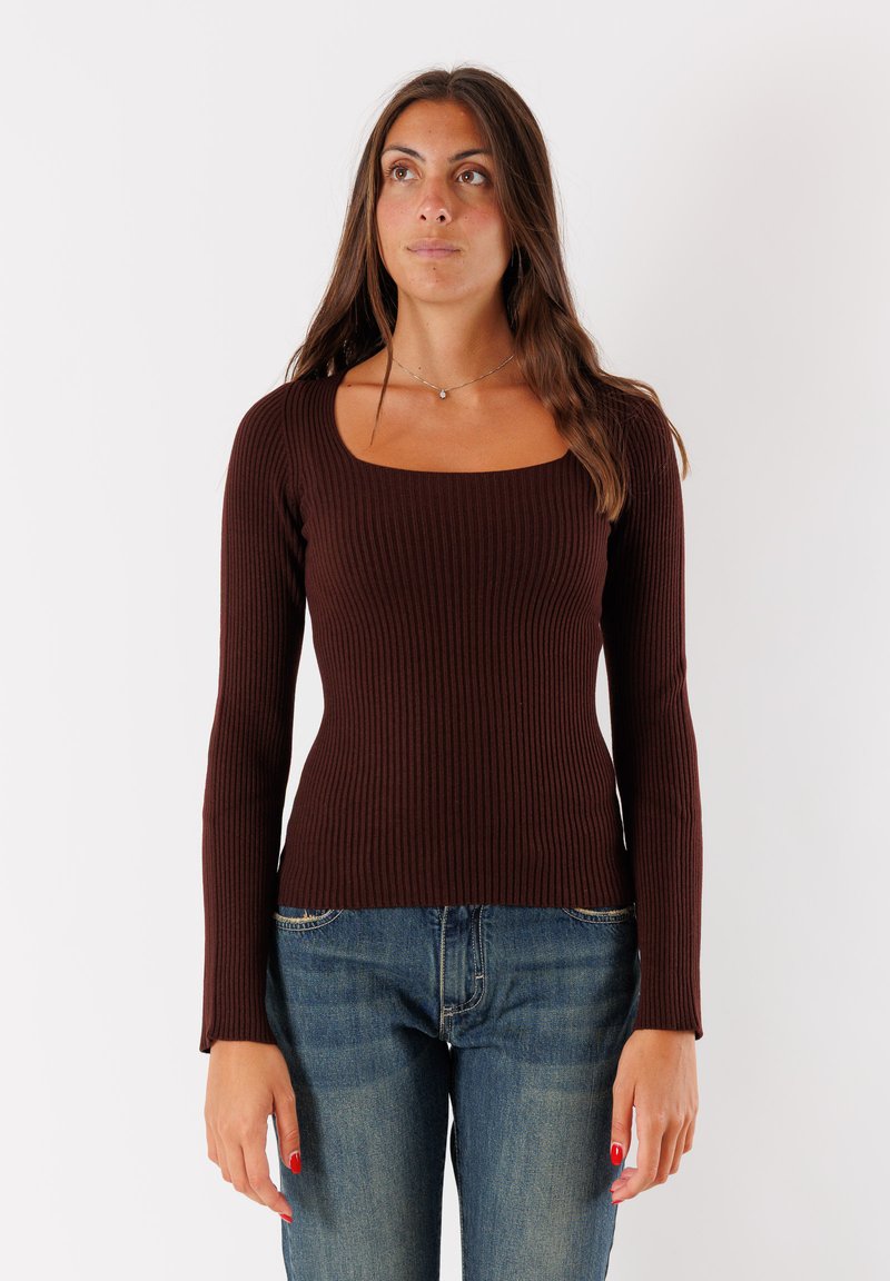 Maglietta marrone a maniche lunghe con scollo quadrato, design aderente e tessuto strutturato, abbinata a jeans di denim blu.