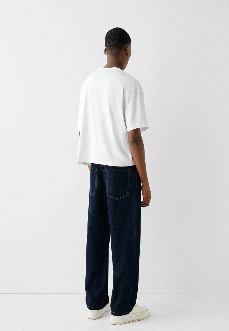 T-shirt en coton blanc, à manches courtes, coupe décontractée, associé à un jean large bleu foncé, avec des poches arrière et des coutures contrastées.