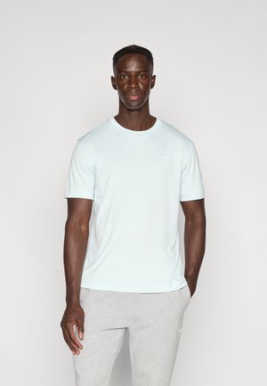 T-shirt bleu clair à manches courtes en tissu lisse, avec un col rond et un petit logo blanc sur la poitrine. Pantalon de survêtement gris.