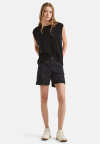 Černý top bez rukávů pletený s ribkovaným lemem, spárovaný s tmavými šortkami s knoflíkovým zapínáním, ohrnutými manžetami a hladkým povrchem látky.