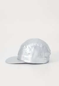 Cappello argentato con un visiera piatta, realizzato in materiale lucido e liscio; presenta dettagli cuciti e due fori di ventilazione sui lati.