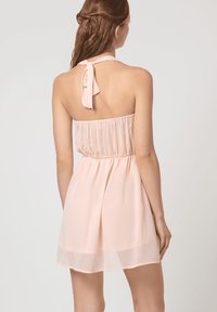 Vestido sin tirantes de color rosa pastel con una cintura elástica y un lazo en el cuello. Tela ligera y fluida; de longitud a la rodilla con un acabado translúcido.
