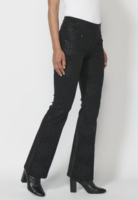 Pantalones acampanados negros con estampado floral, hechos de una tela texturizada. Cuentan con bolsillos frontales y detalles plateados en los bolsillos.