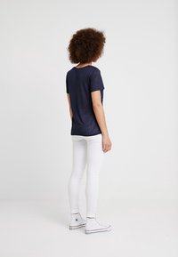 Camiseta de manga corta azul marino hecha de un tejido ligero, combinada con jeans ajustados blancos y zapatillas clásicas blancas.
