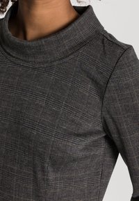 Pull-over gris foncé avec un col haut et un motif écossais texturé. Présente un design ajusté et une texture de tissu lisse.