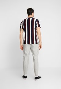 Stribet T-shirt i marineblå, bourgogne og hvid; kortærmet, rund hals. Grå skræddersyede bukser, slim fit, med sorte sneakers på fødderne.