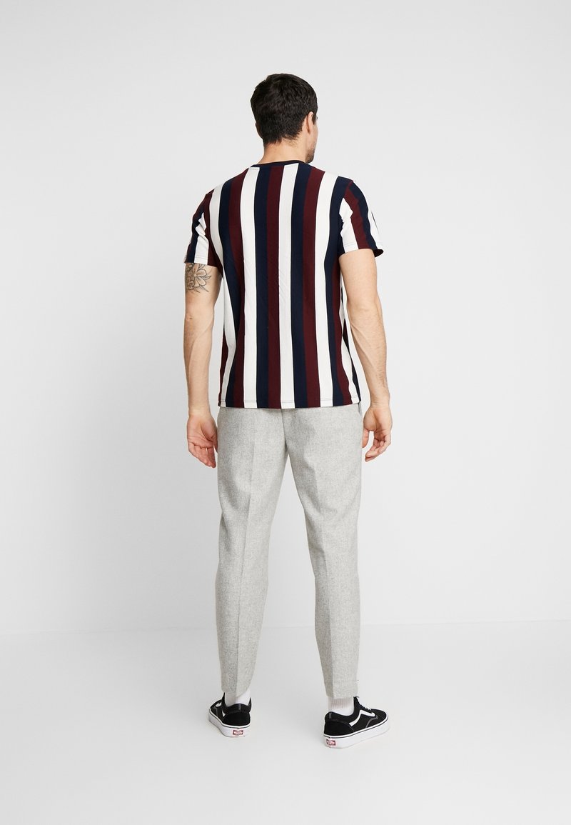 Stribet T-shirt i marineblå, bourgogne og hvid; kortærmet, rund hals. Grå skræddersyede bukser, slim fit, med sorte sneakers på fødderne.