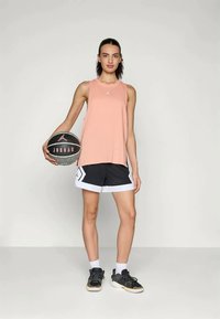 Peach tank top and black shorts with white accents, holding a basketball. The outfit features a relaxed fit and sporty design.