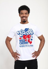 Vit bomulls t-shirt med en grafisk design i blått och rött som visar texten "Try Me Wild Cherry" och körsbär med accenter mot en prickad bakgrund.
