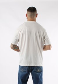 T-shirt bianca in cotone con maniche corte, vestibilità morbida e scollatura rotonda, abbinata a jeans in denim blu con dettagli nelle tasche posteriori.