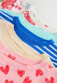 T-shirts en coton posés à plat, présentant des couleurs pastel : rose avec des cœurs rouges, bleu clair, crème, vert menthe, bleu foncé et rayures bleues.