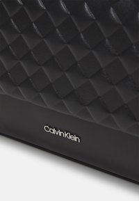 Borsa a tracolla in ecopelle nera con una texture a trapunta, caratterizzata da un logo Calvin Klein in argento. Forma rettangolare con accenti orizzontali.