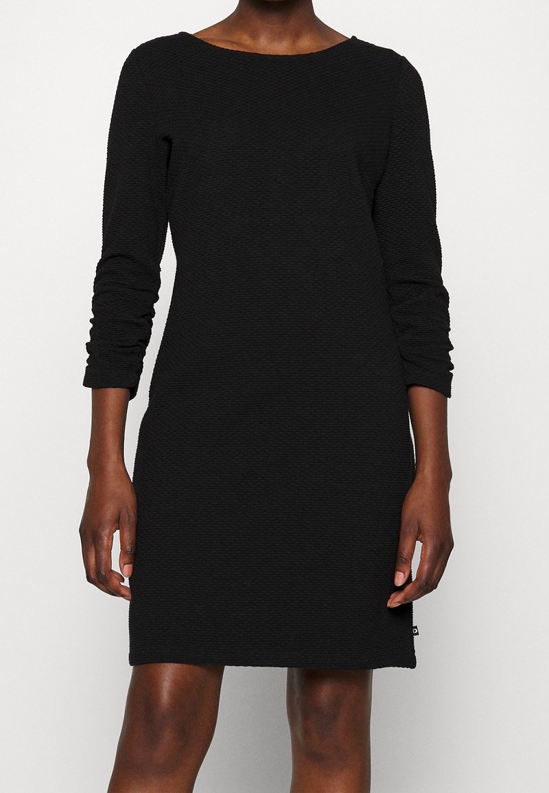 Robe noire à manches longues en tissu texturé, avec un col rond et une coupe droite. Caractéristiques des manches froncées et un petit détail de étiquette sur le côté.