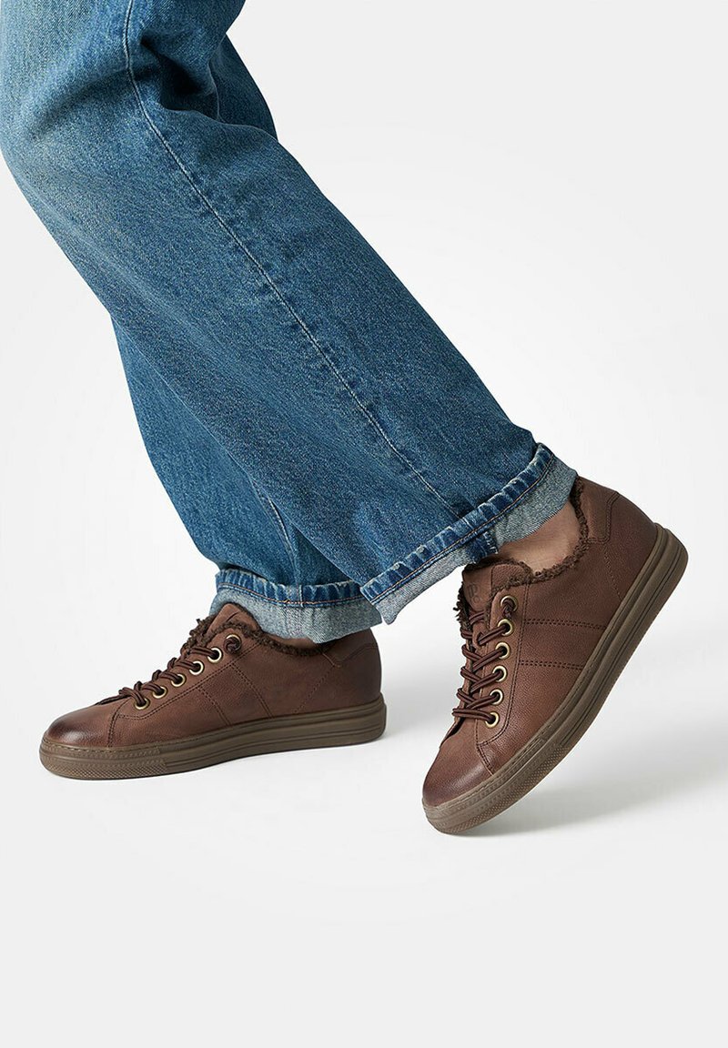 Baskets en cuir marron avec doublure en fourrure, portées avec un jean bleu retroussé, présentées sur des pieds sur fond blanc.