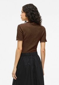 Haut court à manches courtes de couleur marron avec un col froncé, associé à une jupe avec ceinture élastique noire, vu de dos.