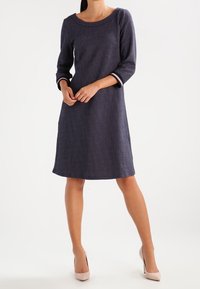 Mörkblå klänning med rund halsringning, trekvart långa ärmar och vitt prickmönster. Slät tyg med kontrasterande ärmuppslag.