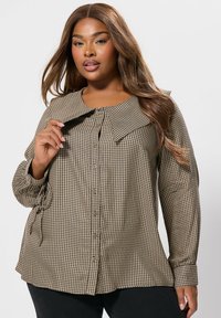 Camicia a quadri marrone e beige con colletto ampio, maniche lunghe e lacci laterali, realizzata in tessuto a fantasia.