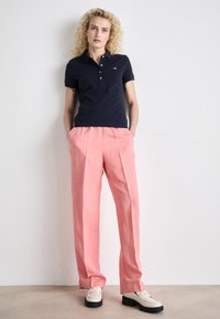 Marineblå polo-skjorte med korte ermer og tre knappåpninger; rosa løse bukser med legg; kremfargede sko med svarte såler.