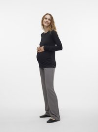 Svart langermet topp med en tettsittende design, kombinert med grå ballongbukser. Modellen står sidelengs og viser en fremtredende mage. Svart slip-on sko.