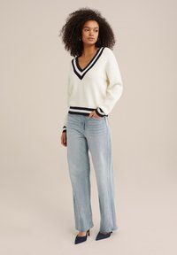 Suéter de punto blanco con rayas navy en el escote en V y los puños, combinado con jeans rectos de color azul claro y tacones de punta navy.