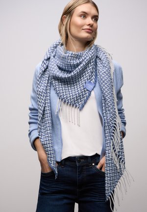 Blue patterned scarf with fringed edges, made of soft fabric; worn over a light blue top, paired with dark jeans.
