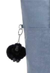 Borsa grigia realizzata in tessuto resistente, con un portachiavi a forma di scimmia nera in peluche attaccato da un anello di metallo. Cuciture in evidenza visibili sulla superficie.