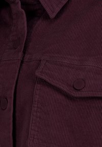 Burgundy corduroy fabric with vertical ribbed texture, featuring a collar and two front flap pockets with round black buttons.