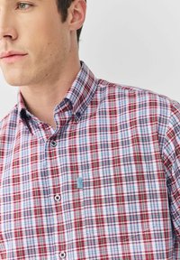 Rot-blau kariertes Hemd zum Knöpfen mit klassischem Kragen, Taschen-Detail und kontrastierenden Knöpfen. Der Stoff wirkt leicht und glatt.