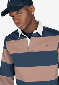 Polo rugby a righe nei colori navy, rosa e bianco, con colletto, logo ricamato e una placca dei bottoni funzionale.