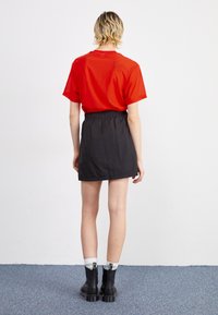 Röd kortärmad T-shirt i kombination med en svart mini kjol med elastisk midja, bärs med svarta ankelstövlar och randiga strumpor.