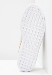 Baskets beige avec une tige en daim texturé et une semelle en caoutchouc blanche ornée d'un motif géométrique. Logo visible sur le côté de la semelle.