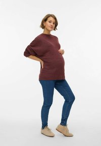 Bordo pleteni džemper s okruglim izrezom, širokim krojem i rukavima tri četvrtine, u kombinaciji s plavim uskim trapericama i bež cipelama.