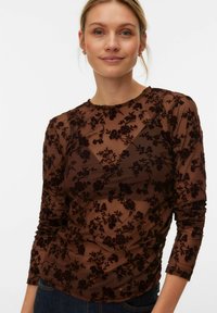 Haut à manches longues en maille marron à motif de fleurs en velours. Il a un col rond et une coupe ajustée avec un détail froncé subtil.