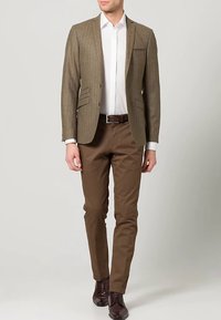 Brauner Nadelstreifenblazer, weißes Hemd, braune Hose, strukturiertes Gewebe, brauner Ledergürtel, dunkle Schuhe, schlanke Passform.