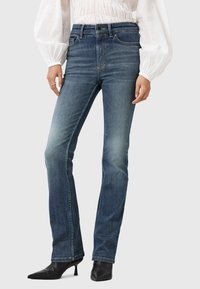 Hoge taille blauwe denim jeans met een slim fit, een lichte vervaging, voorzakken en stikdetails. Gecombineerd met zwarte puntenhakken.