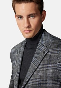 Szary marynarka w kratę z niebieskimi akcentami, wyposażona w klapy notch i teksturowany materiał, noszona na czarnym swetrze z golfem.