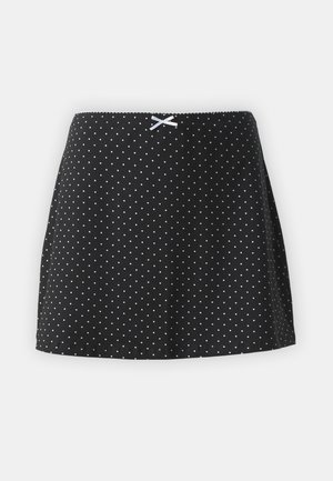 Melnā svārku ar baltām punktēm, ar savilktu jostas daļu un nelielu dekoratīvu lentīti priekšpusē. Īss un izlocīts dizains.