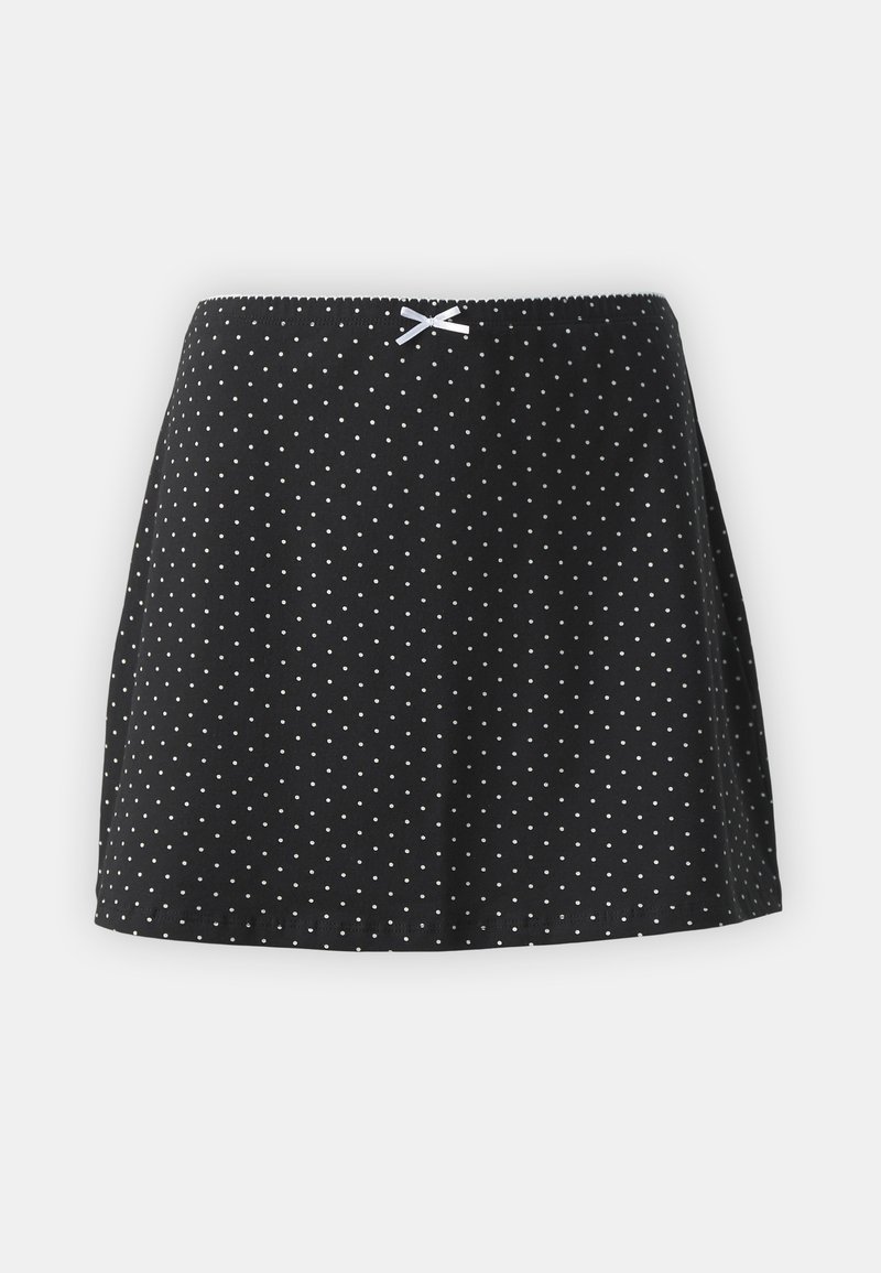 Jupe noire à pois blancs, avec une taille froncée et un petit ruban décoratif sur le devant. Design court et évasé.