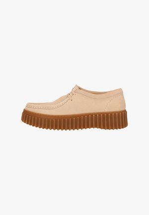 Beige suede shoe with a round toe, featuring a thick brown rubber sole with prominent ridges and lacing at the front.
