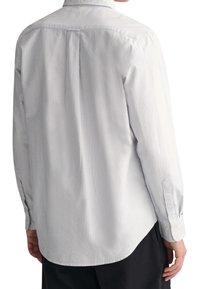 Lichtblauw en wit gestreepte lange mouw shirt, gemaakt van stof met een zachte textuur. Voorzien van een button-down kraag en enkele knopenmanchetten.