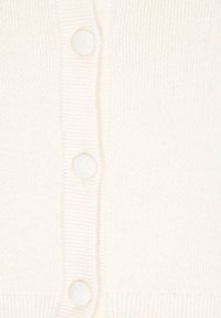 Bílý pletený cardigan s ribkovanou strukturou, jehož přední část zdobí pět kulatých knoflíků a vypasovaný pas. Měkký a lehký materiál.