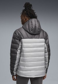Padded jacket w kolorze szarym u góry i jasnoszarym u dołu. Posiada kaptur, puchowy fason oraz przeszywane linie dla tekstury.