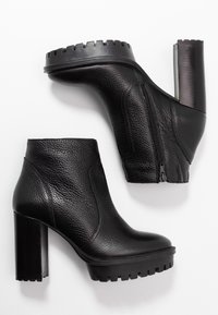 Botas negras hasta el tobillo hechas de cuero texturizado con una suela gruesa y estriada y un tacón de bloque alto y suave. Detalle de cremallera lateral presente.