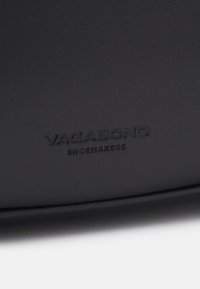 Le matériau en cuir noir présente une texture lisse avec un grain subtil. Le nom de la marque "VAGABOND SHOEMAKERS" est embossé en bas.