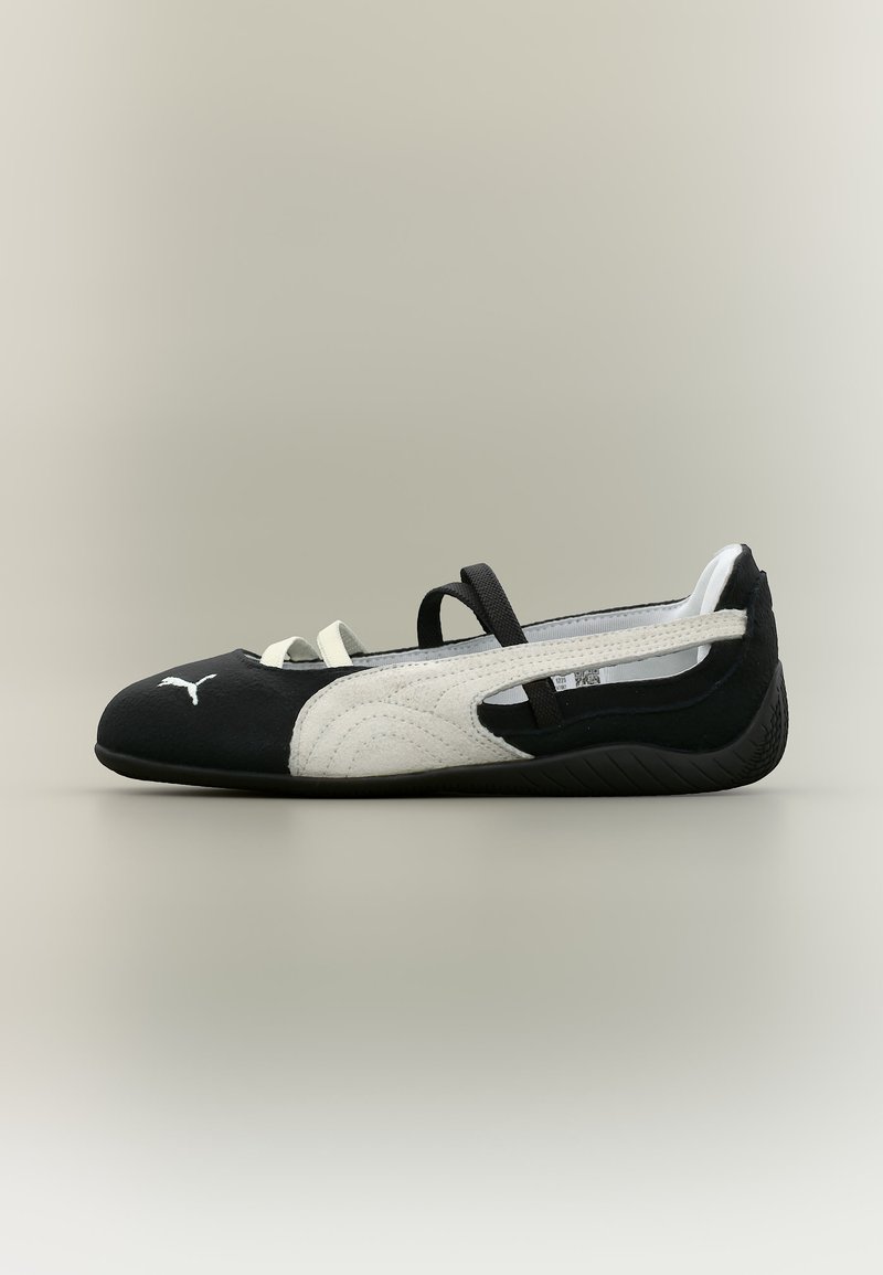 Μαύρο και άσπρο μπαλαρίνα παπούτσι Puma με ελαστικούς ιμάντες και λαστιχένια σόλα, πλευρική όψη σε απλό φωτεινό φόντο.
